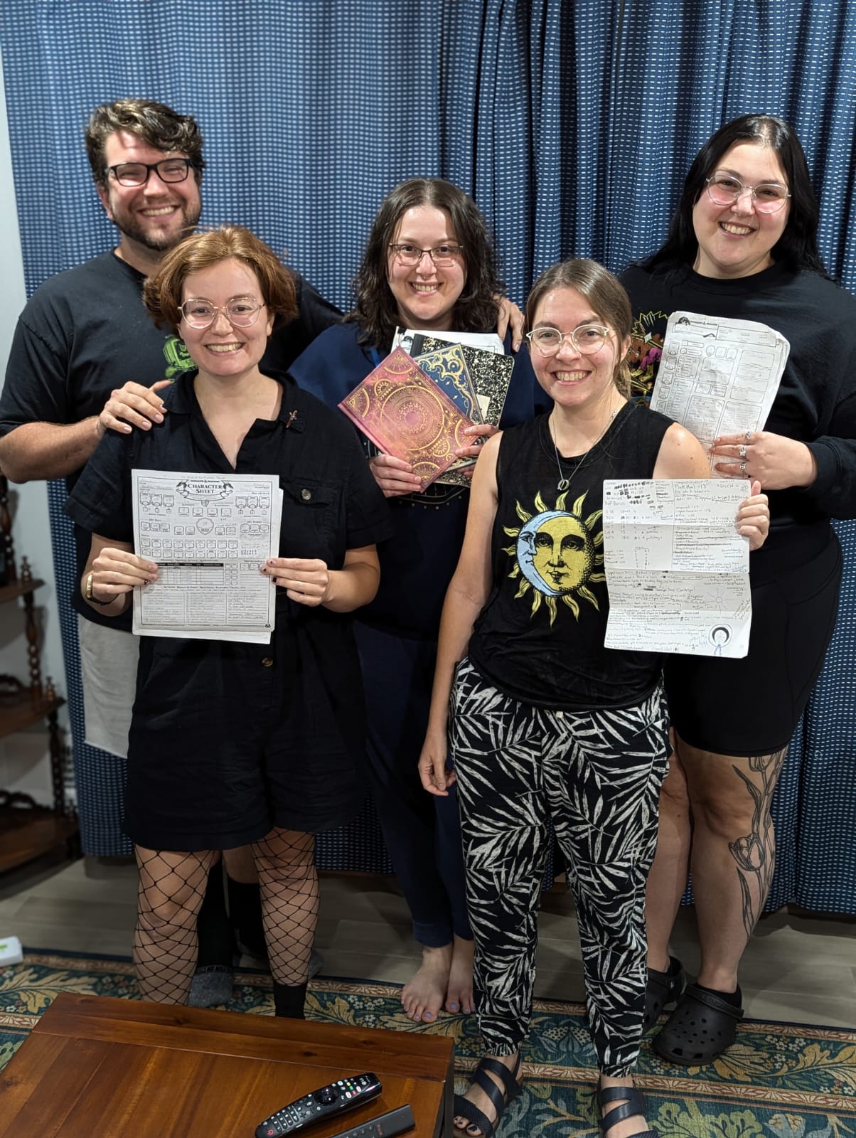 Five people standing in a group, four of whom are holding up their dungeons and dragons character sheets.