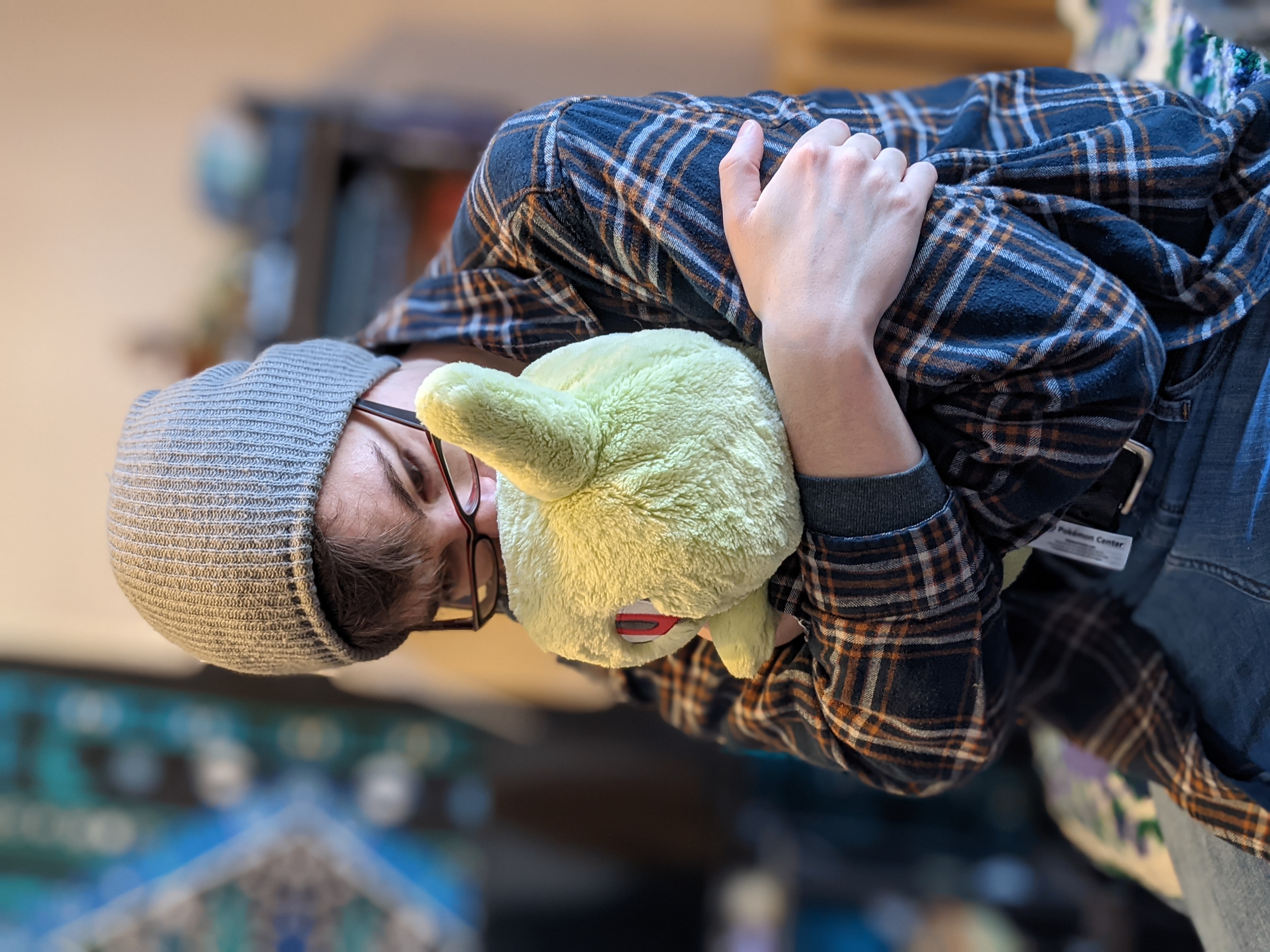 A photo of a person sitting on a bed hugging a larvitar plushie.