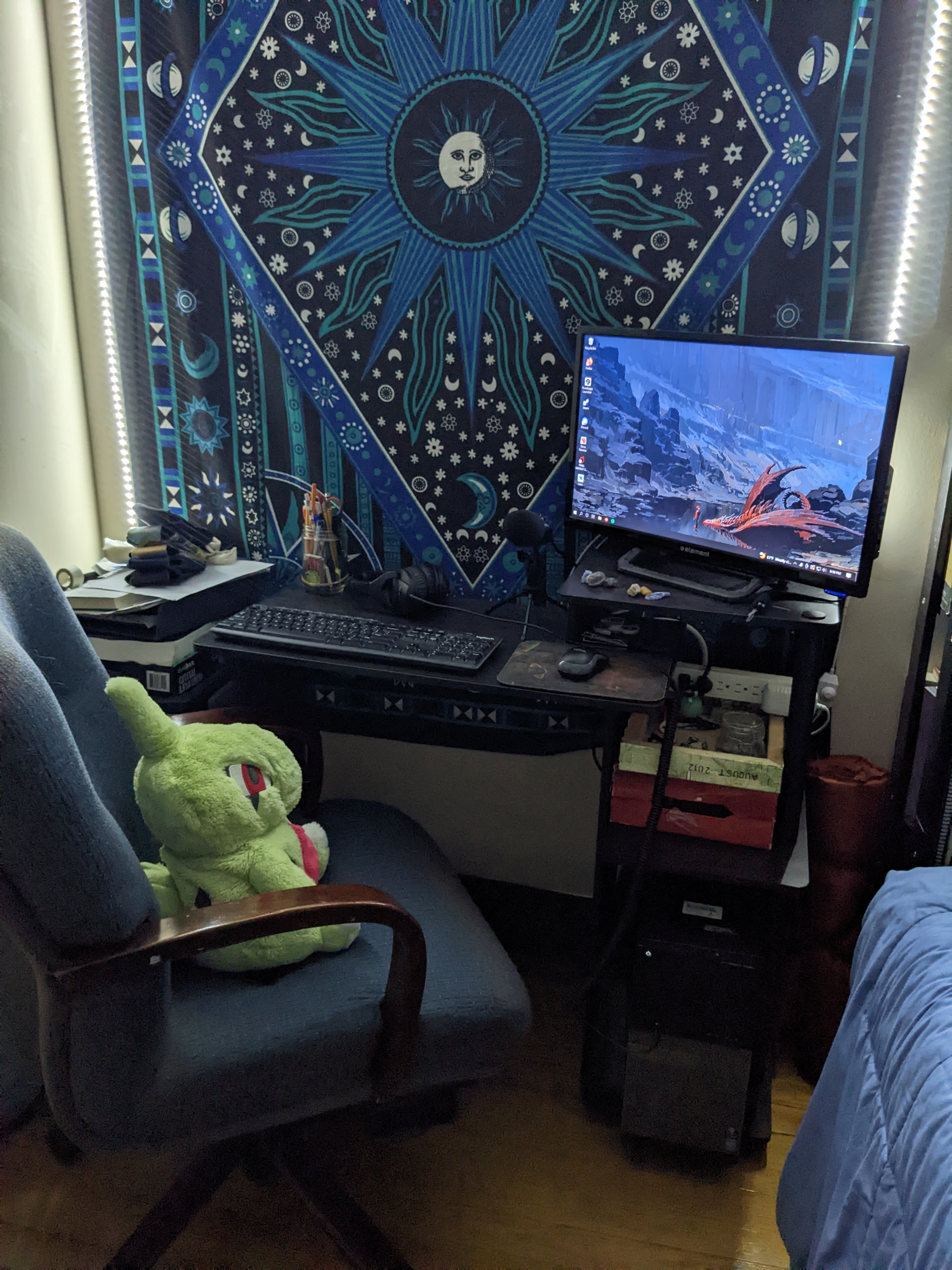 A photo of a desk set up, in front of a tapestry with the moon on it, surrounded by RBG white lights.